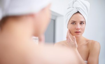 A woman looking in her bathroom mirror with a towel on her head